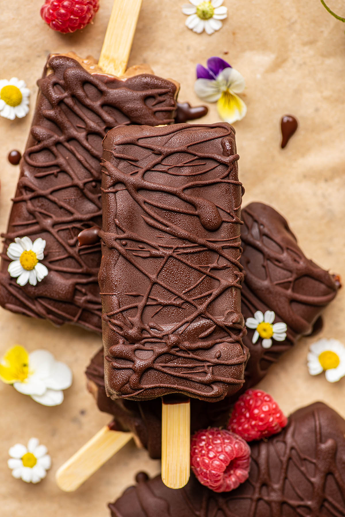 Dark chocolate coated popsicles on parchment paper with flowers and berries.