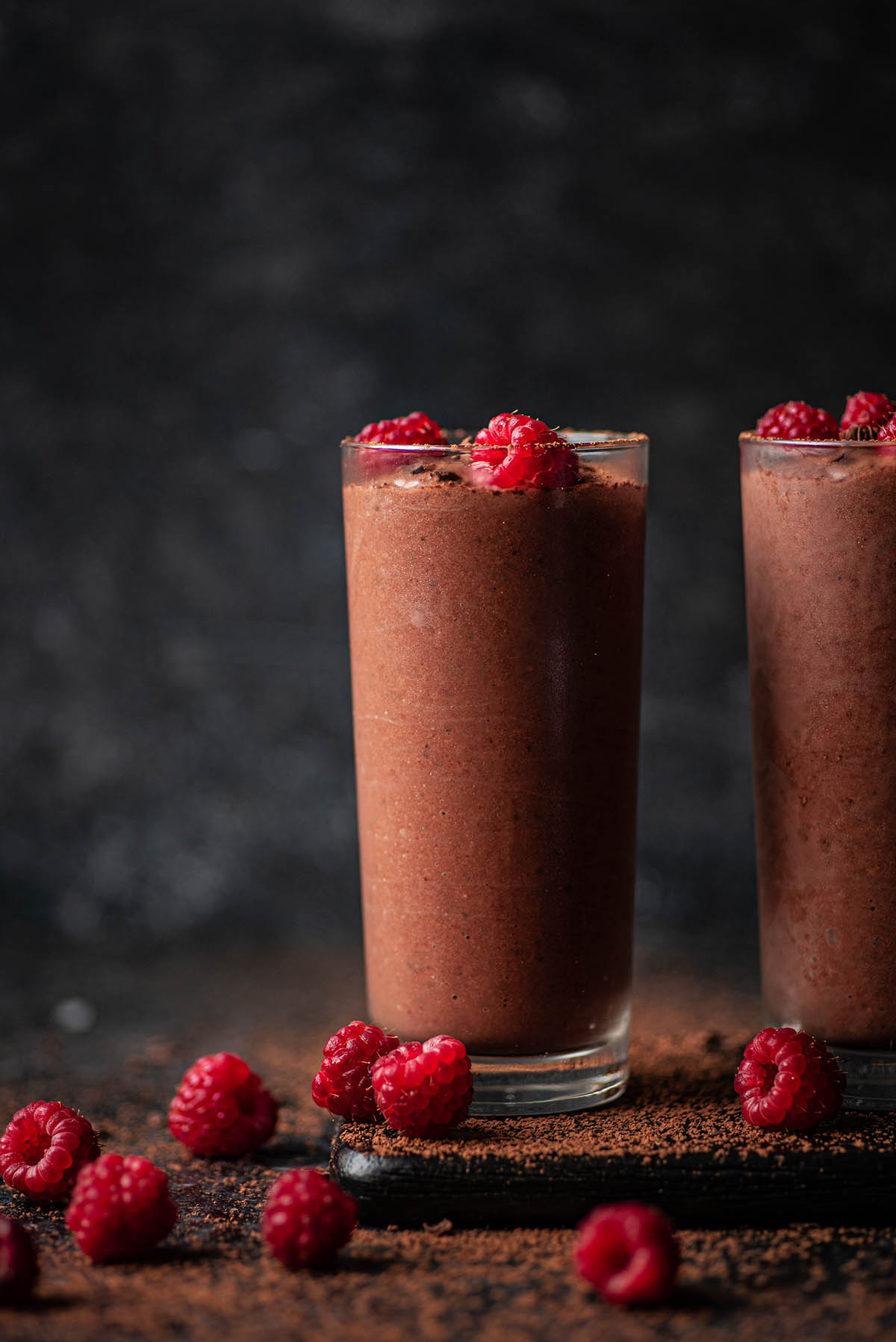 Two glasses of chocolate smoothie with raspberries.