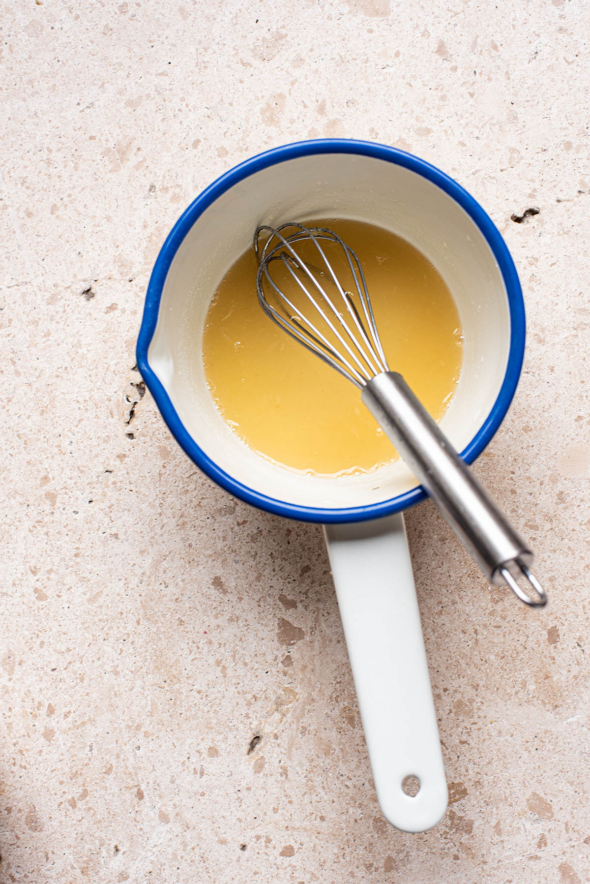 A small saucepan holding a whisk and a yellow lemon and honey mixture.