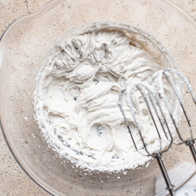 Whipped cream in a large glass bowl with an electric mixer.