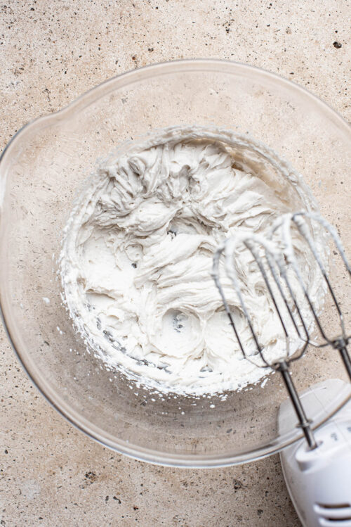 Whipped cream in a large glass bowl with an electric mixer.