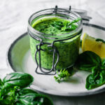 A jar of tahini on a plate with basil in front of it.