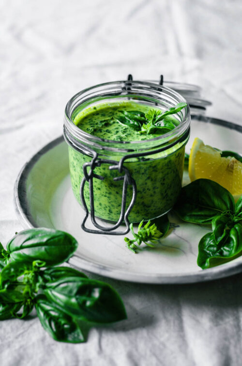 A jar of tahini on a plate with basil in front of it.