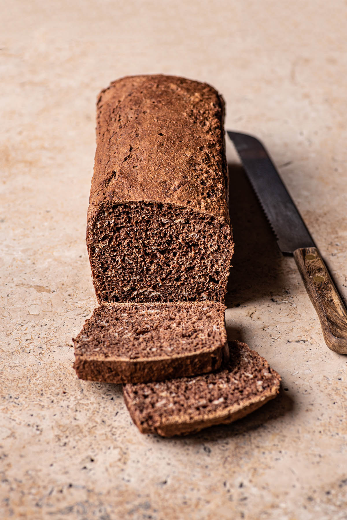A loaf of dark rye bread with two slices cut.