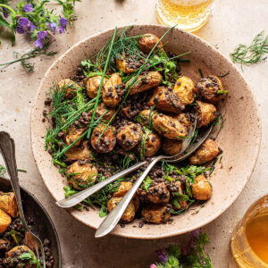A large bowl of potato salad with lentils and herbs with two serving spoons.