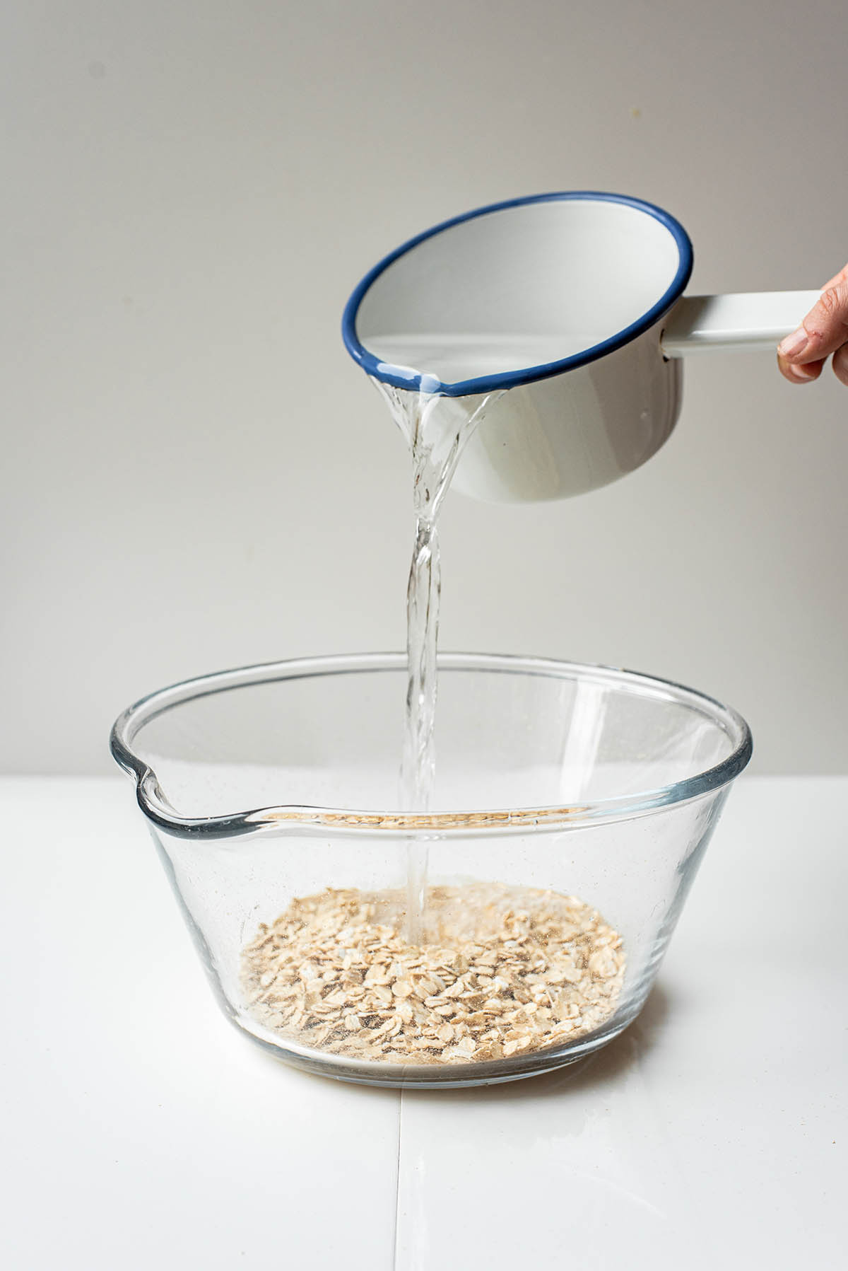 A small saucepan of hot water being poured into a large bowl with oats.
