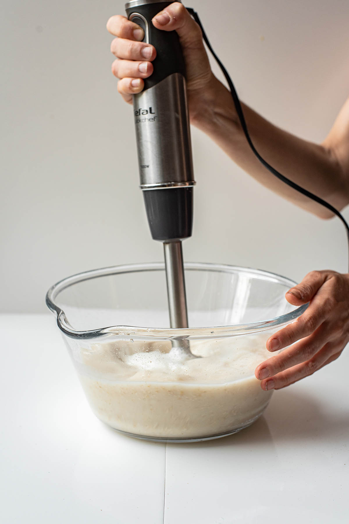 Blending oat milk with an immersion blender in a glass bowl.