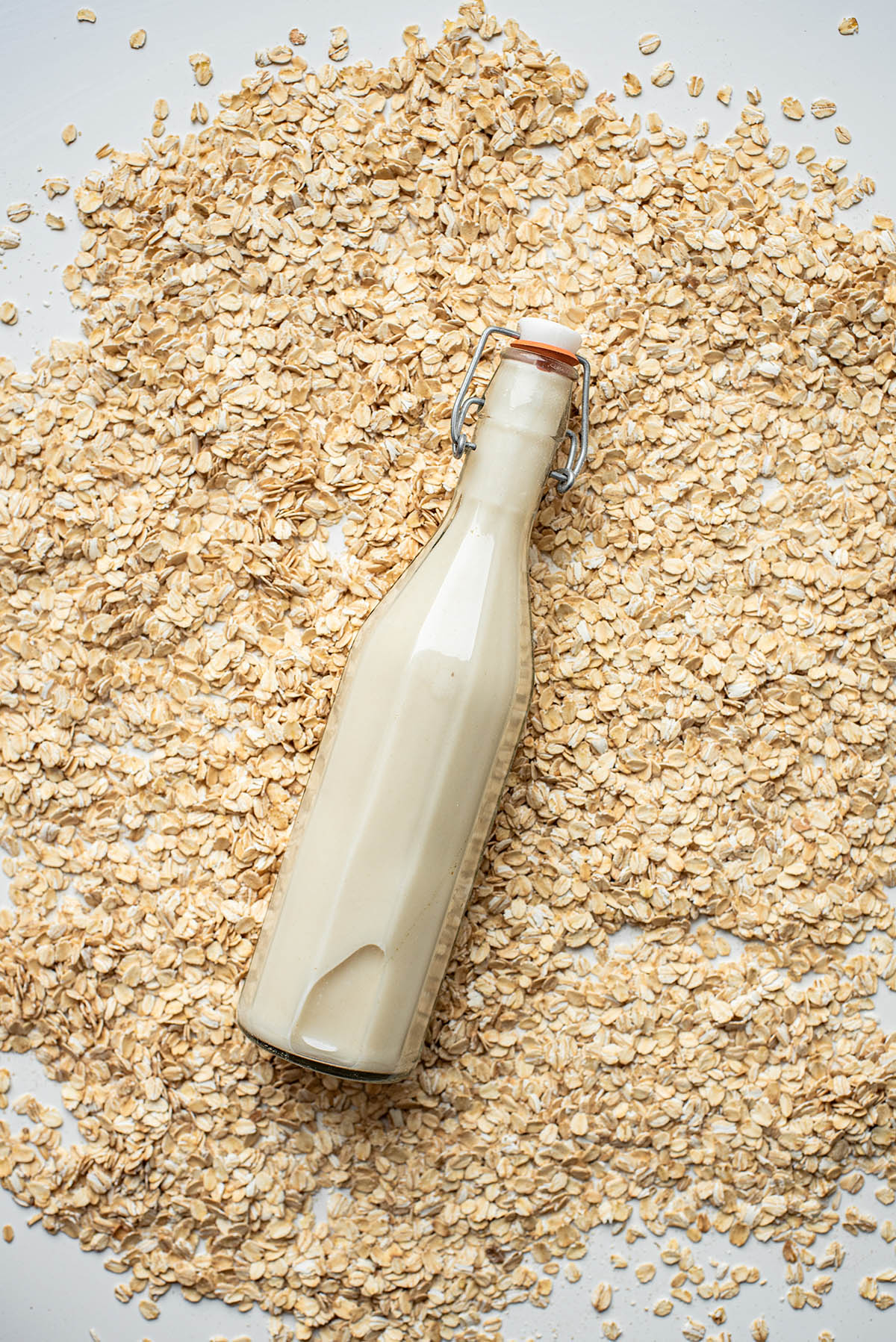 Oat milk in a flip-top glass bottle lying in a pile of oats.