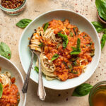 A bowl of lentil bolognese with pasta and basil.