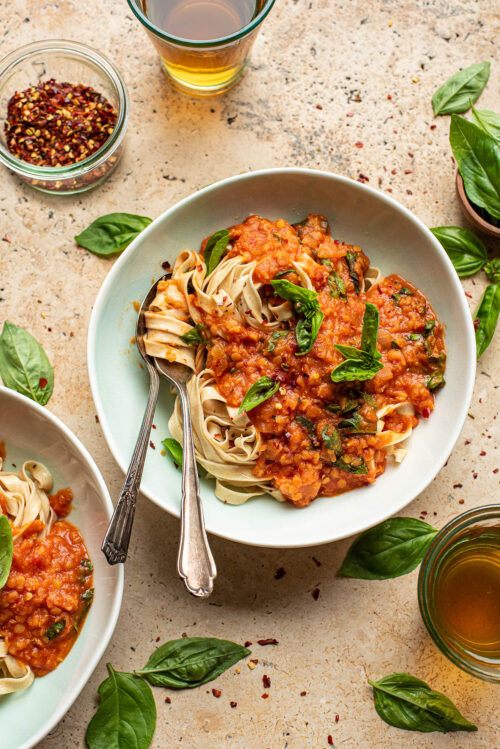 A bowl of lentil bolognese with pasta and basil.