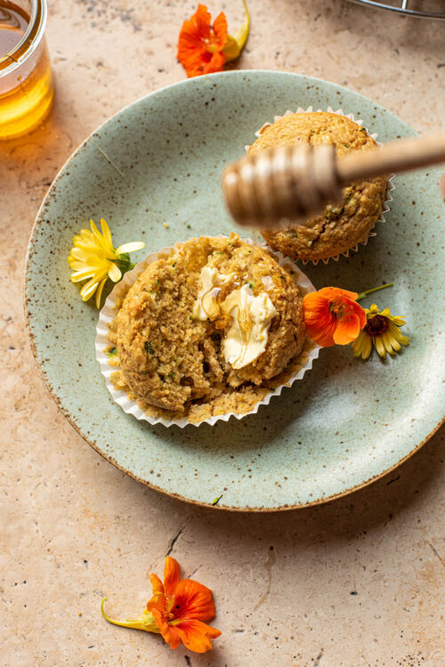 Honey being drizzled onto a sliced cornbread muffin.
