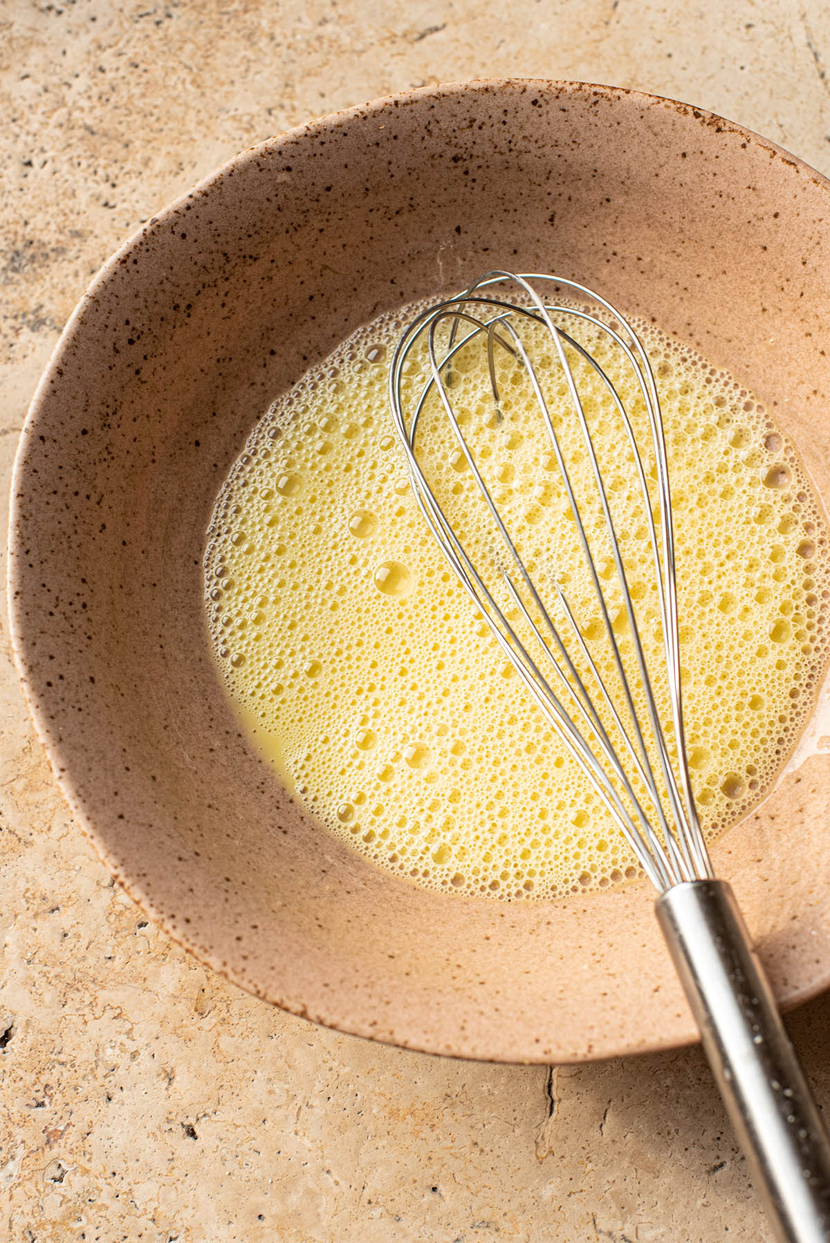 Whisked eggs and wet ingredients in a bowl with whisk.