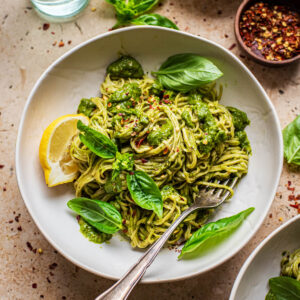 A bowl of pasta with green sauce and basil.