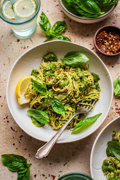 A bowl of pasta with green sauce and basil.