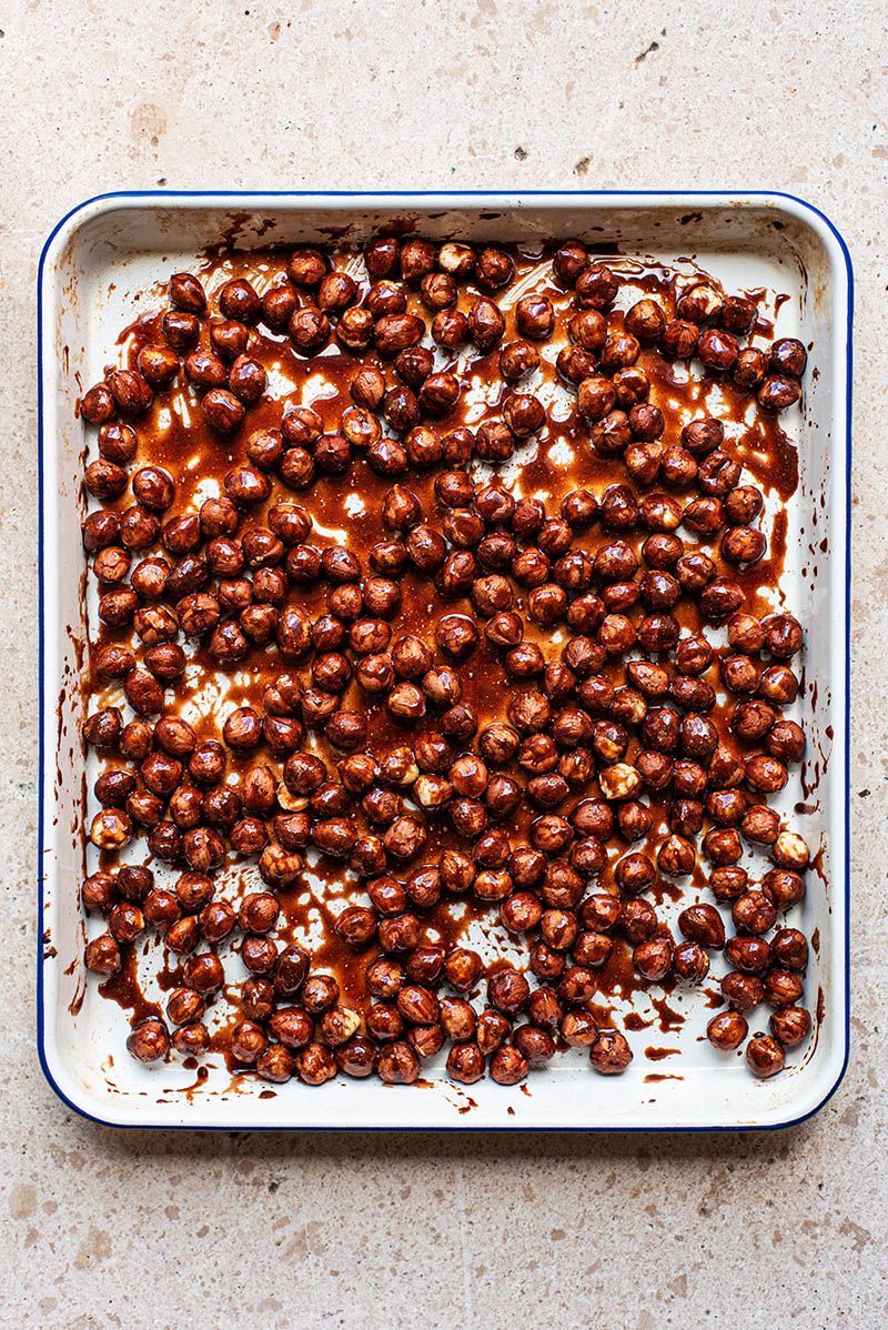 Hazelnuts mixed with date syrup, cinnamon, and salt on a baking sheet.