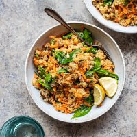 Two bowls of quinoa salad with two glasses of water.