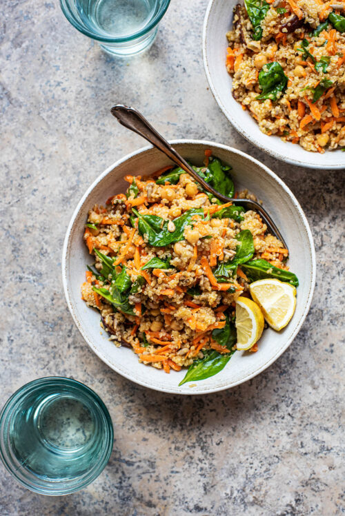 Two bowls of quinoa salad with two glasses of water.