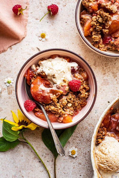 A small bowl of plum crisp with ice cream and raspberries.