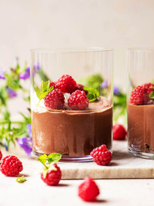 Vegan chocolate mousse in glasses with cream and raspberries.