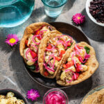 Three cauliflower tacos topped with pickled red onions.