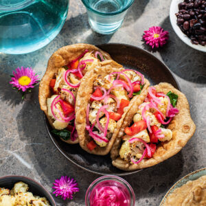 Three cauliflower tacos topped with pickled red onions.