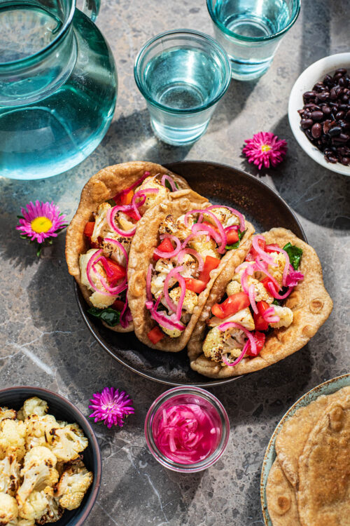 Three cauliflower tacos topped with pickled red onions.
