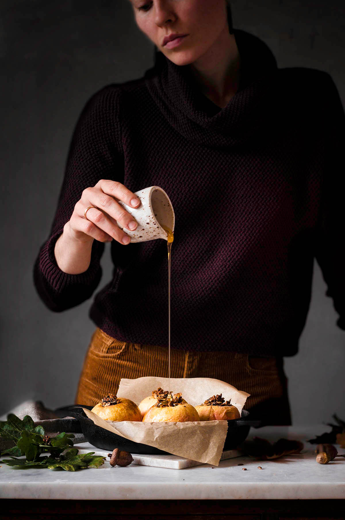 Woman pouring maple syrup onto baked apples.