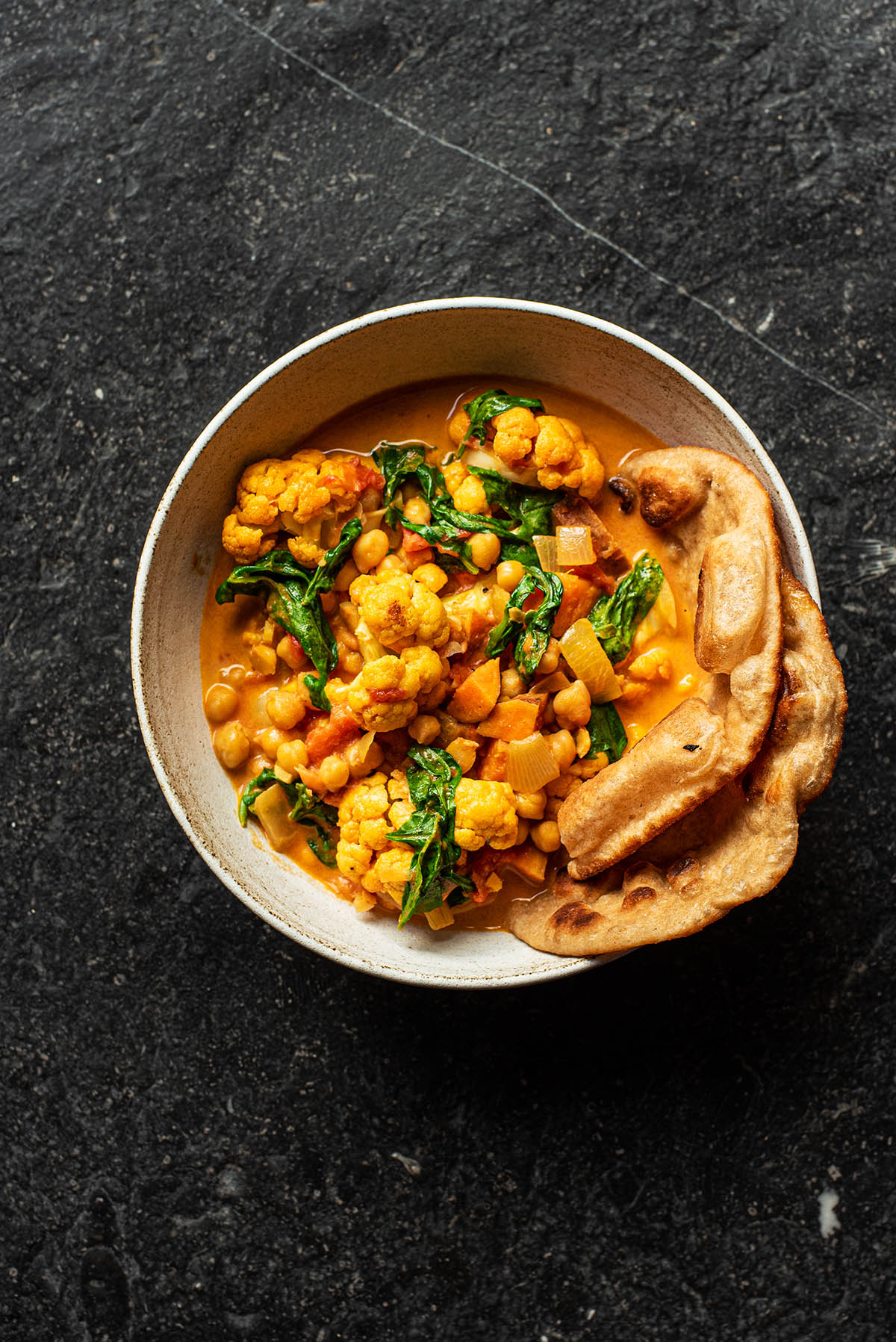 A bowl of cauliflower curry with naan tucked in.