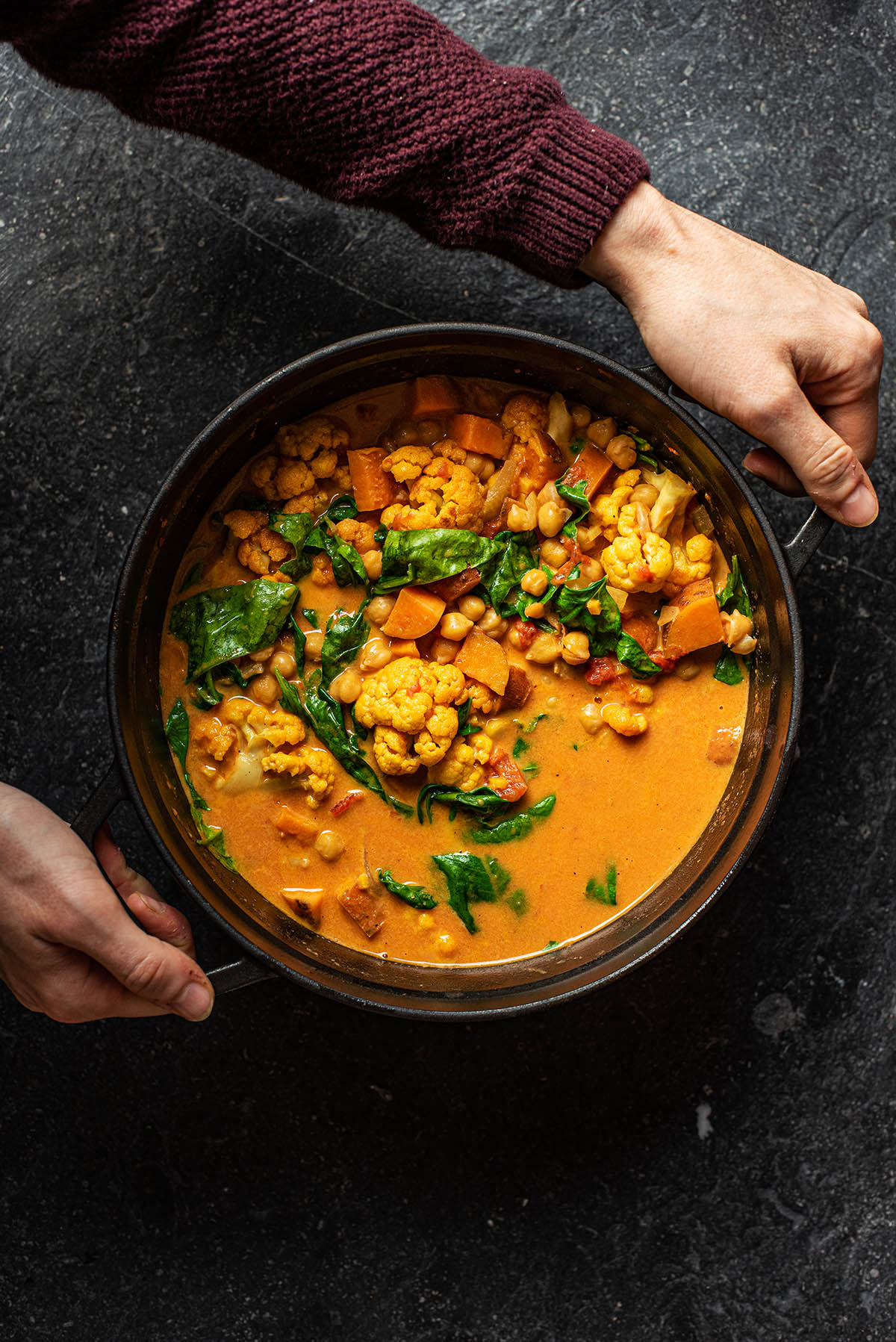 Hands lifting the pot of curry.