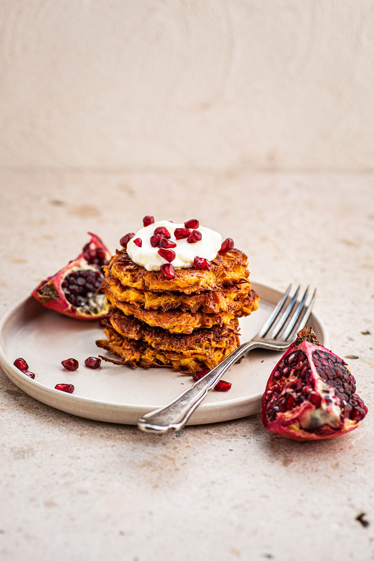 Latkes on a plate with pomegranate in fore and background.