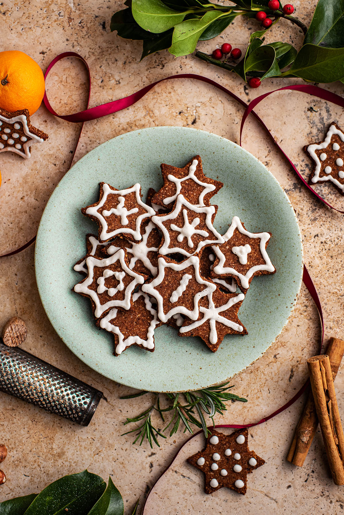 A plate of cookies surrounded with spices, oranges, ribbon, and greenery.