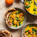 Bowls of pumpkin curry with naan and small pumpkins around.
