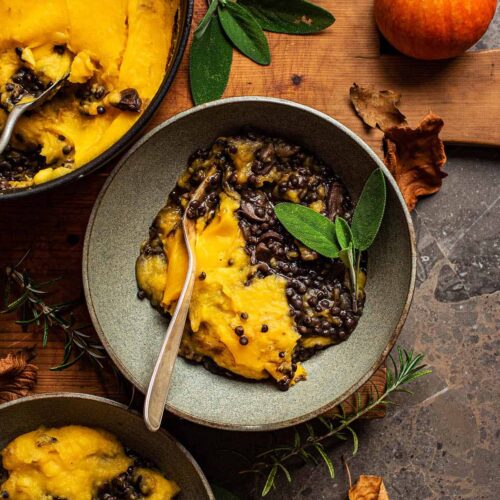 Two bowls of pumpkin lentil shepherd's pie with the pot to the side.