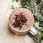 A mug of hot chocolate with a foamy top and some shaved chocolate on top.