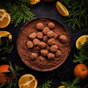 Bowl of truffles surrounded by oranges and greenery.