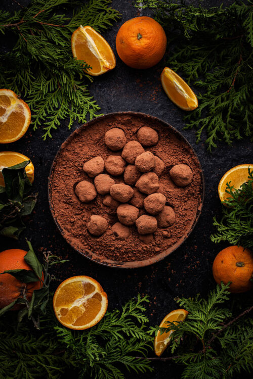 Bowl of truffles surrounded by oranges and greenery.