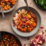 Two bowls of carrot chickpea stew with greens and pomegranate.