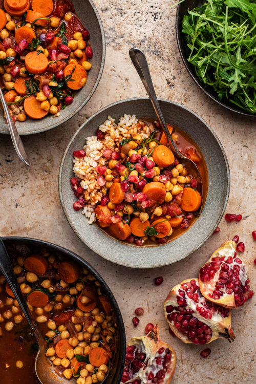 Two bowls of carrot chickpea stew with greens and pomegranate.