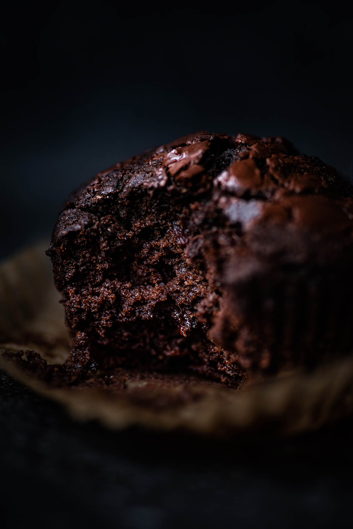 A chocolate muffin with a bite taken out on the muffin liner.