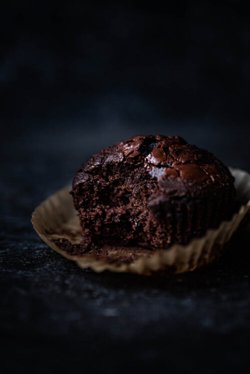 A chocolate muffin with a bite taken out on the muffin liner.