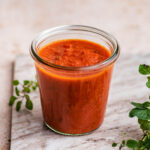 Tomato sauce in a glass jar with oregano around.