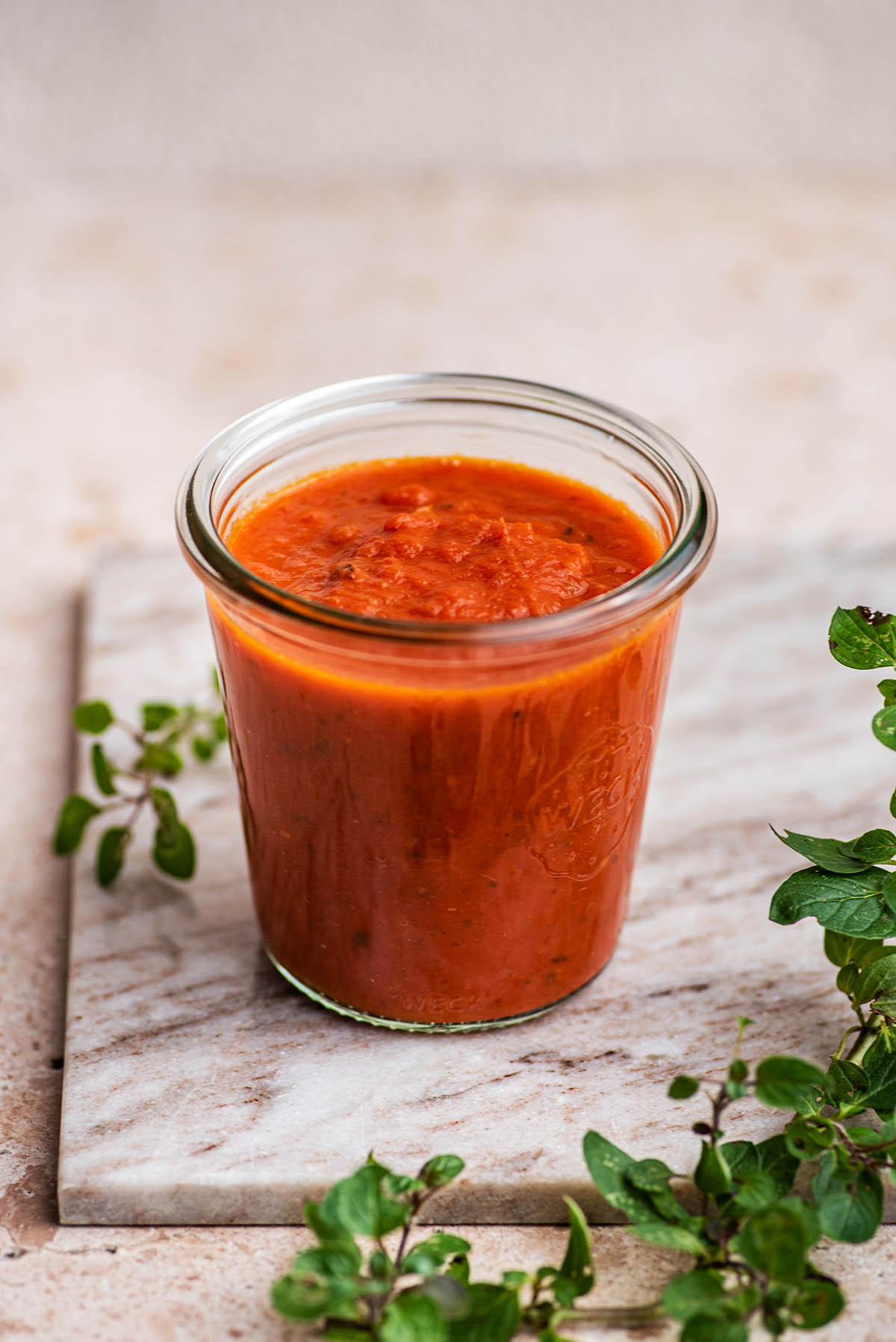 Tomato sauce in a glass jar with oregano around.