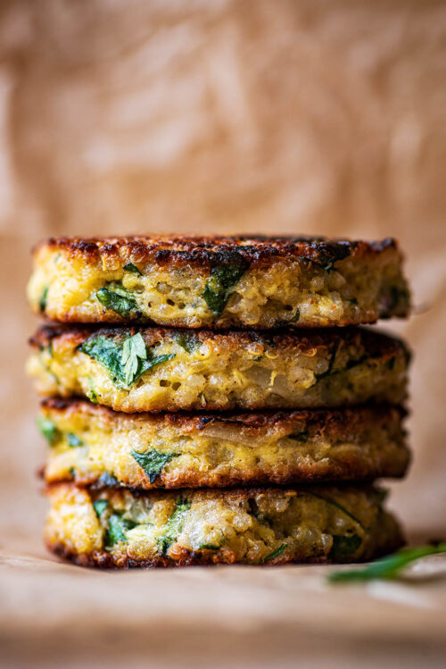 A stack of four quinoa patties on baking paper.