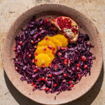 A shallow bowl of red cabbage salad with orange and pomegranate.