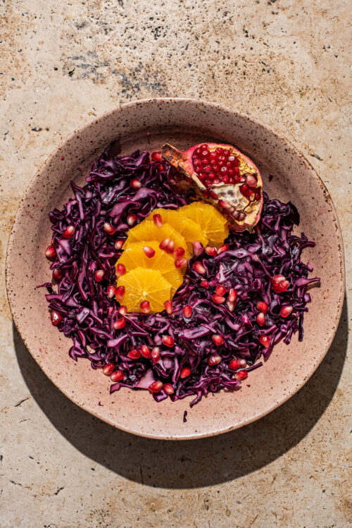 A shallow bowl of red cabbage salad with orange and pomegranate.