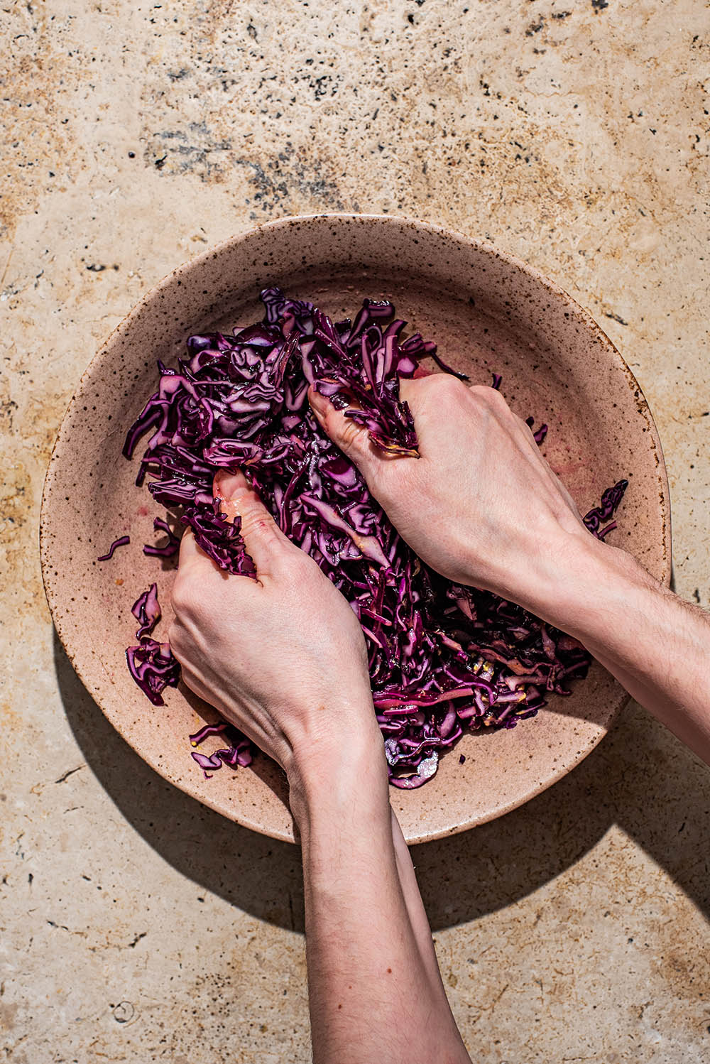 Woman's hands massaging the cabbage in a bowl.