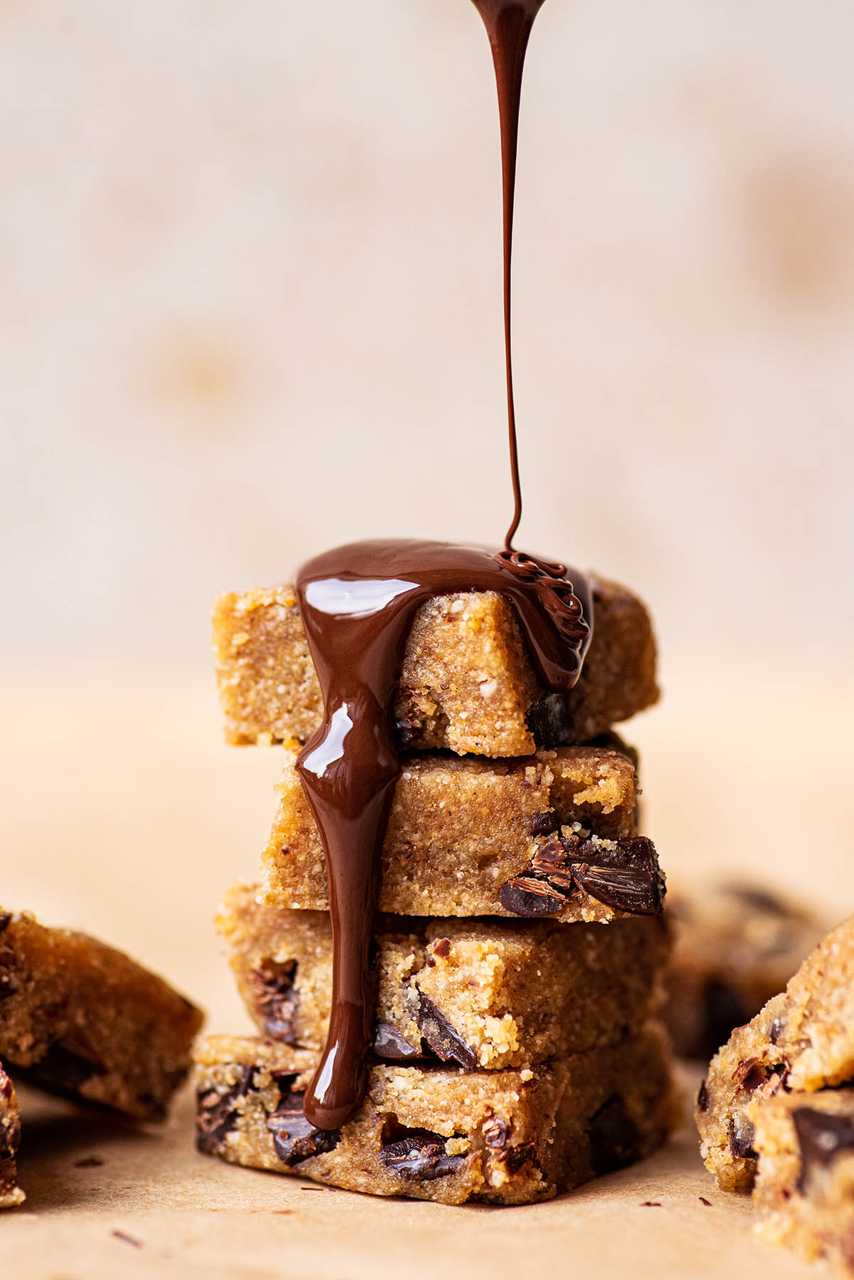 Pouring melted chocolate onto a stack of cookie dough squares.
