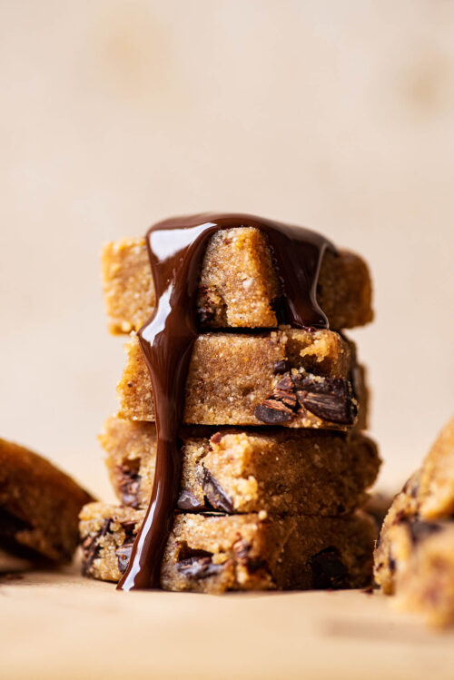 Melted chocolate topped stack of gluten free cookie dough squares..