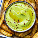 A dish of avocado aioli with roasted potato wedges.