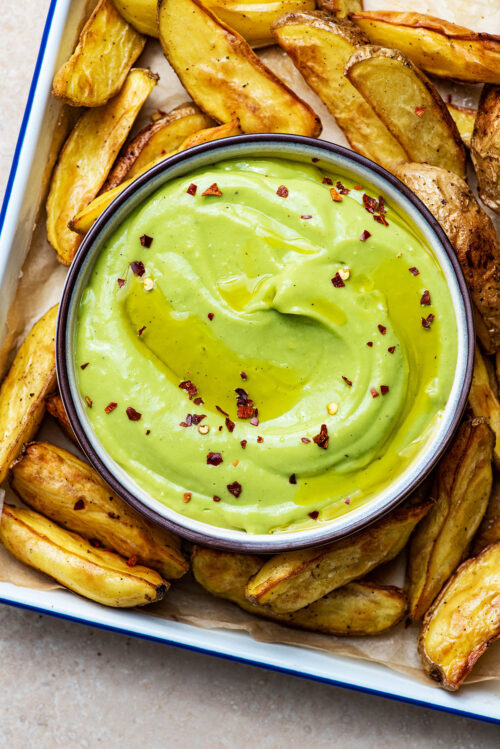 A dish of avocado aioli with roasted potato wedges.